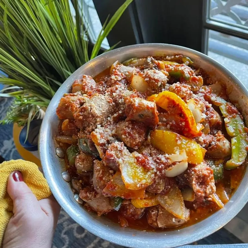 A large metal bowl of Rig A' Tony's Italian sausage, peppers, and onions, topped with cheese.