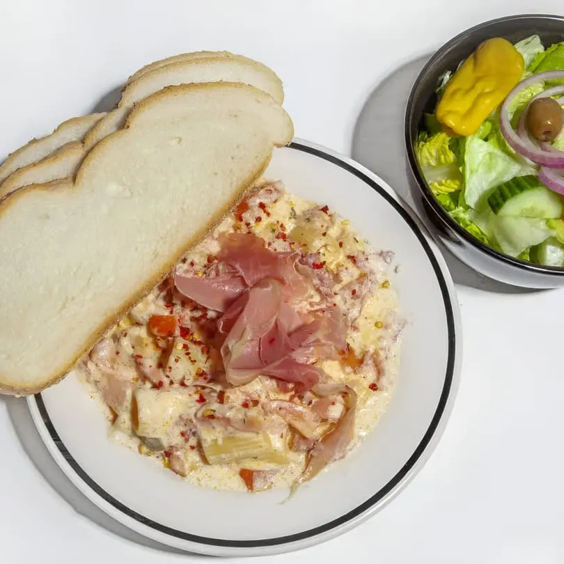Creamy pasta with prosciutto and red pepper flakes, served with sliced bread and a side salad.