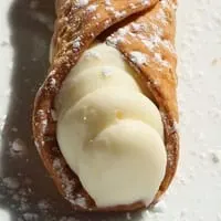 A close-up of a Rig A' Tony's cannoli, filled with creamy white ricotta and dusted with powdered sugar.