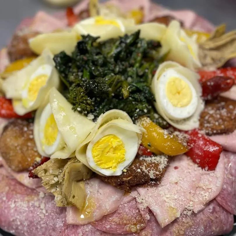 A platter of Italian antipasto with meats, cheeses, eggs, vegetables, and fried items.