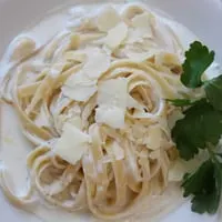 Creamy fettuccine alfredo with shaved parmesan cheese and a sprig of parsley.